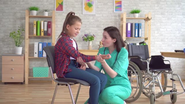 doctor examines the hand of a teenage girl in a wheelchair after an injury