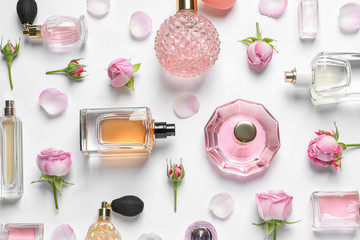 Different perfume bottles and flowers on white background, top view