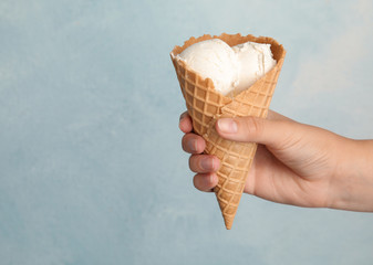 Woman holding delicious ice cream in wafer cone on light blue background, closeup. Space for text