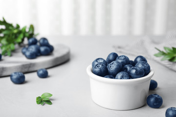 Bowl of tasty blueberries on grey table, space for text
