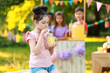 Fototapeta premium Cute little girl drinking natural lemonade in park, space for text. Summer refreshing beverage