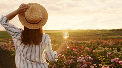 Woman with glass of wine in rose garden on sunny day. Space for text