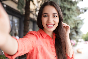 Beautiful young woman taking selfie outdoors on sunny day