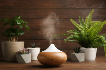 Composition with modern essential oil diffuser on wooden table against brown background, space for...