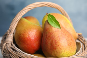 Ripe juicy pears in wicker basket against blue background, closeup