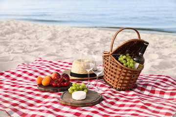 Checkered blanket with picnic basket and products on sunny beach
