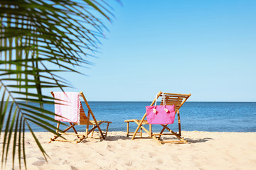 Empty wooden sunbeds and beach accessories on sandy shore