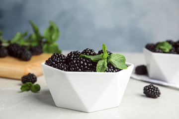 Fototapeta na wymiar Bowl of tasty blackberries on grey marble table