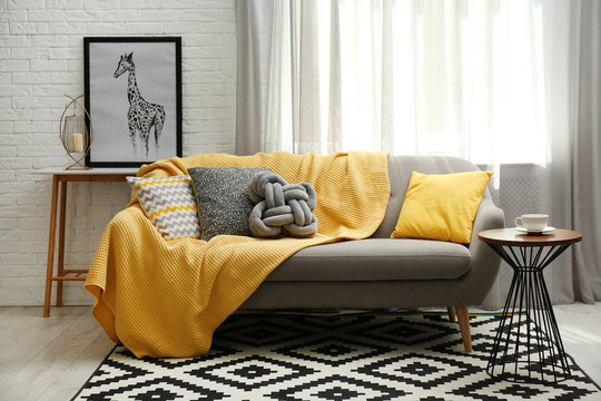 Stylish living room interior with soft pillows and yellow plaid on sofa