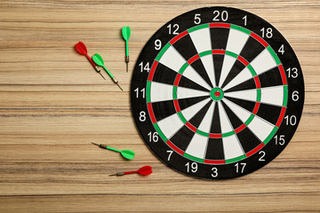 Dart board with color arrows on wooden background, top view. Space for text