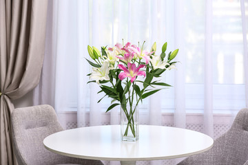 Vase with bouquet of beautiful lilies on white table indoors