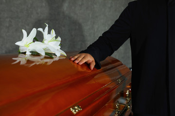 Young man near casket with white lilies in funeral home