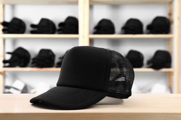 Blank black cap on wooden table in store. Mock up for design