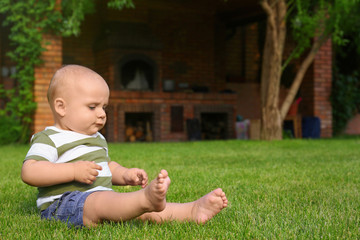 Adorable little baby sitting on green grass outdoors