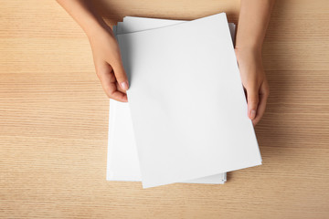 Obraz premium Woman holding blank paper sheets for brochure at wooden table, top view. Mock up