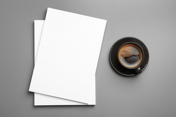 Blank paper sheets for brochure and cup of coffee on grey background, flat lay. Mock up