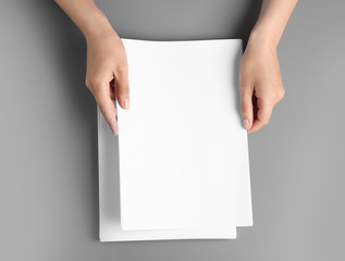 Woman holding blank paper sheets for brochure at grey table, top view. Mock up