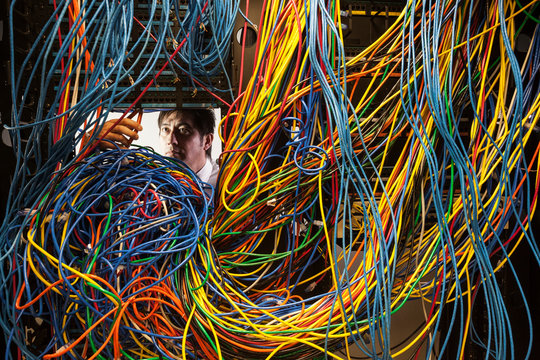 Technician working on tangled mess of cat 5 cables in server room