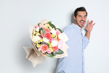 Young handsome man with beautiful flower bouquet on light background