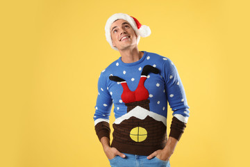 Man in Christmas sweater and Santa hat on yellow background