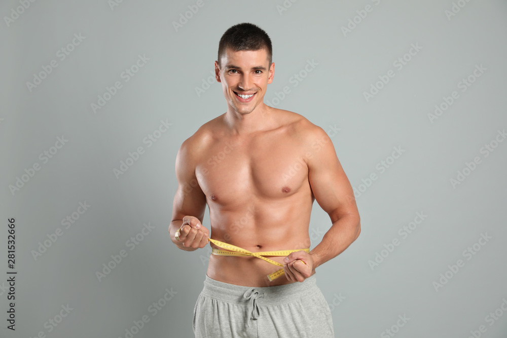 Poster Young man with slim body using measuring tape on grey background