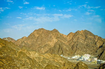 A small town surrounded by large pointy mountains on a clear sunny day. From Muscat, Oman.