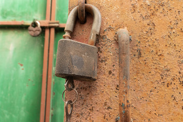 old rusty padlock with two keys hanging on a rusty iron door on the background of a green iron gate with a closed padlock