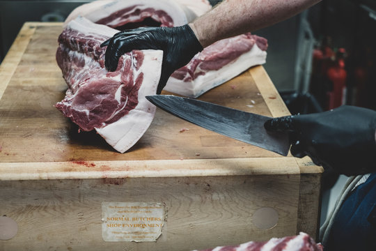 Butcher wearing black gloves cutting pork ribs on butcher's block