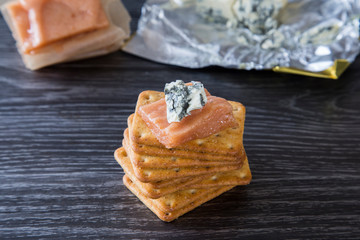 Delicious homemade quince paste served with creamy blue vein cheese and wheat crackers. On a dark background, nice contrast. Great combination of sharp cheese with sweet paste on a salty cracker.