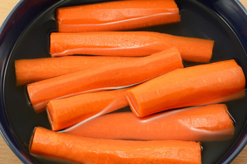 Peeled and halved raw carrots in bowl of fresh water to keep fresh and crisp in refrigerator