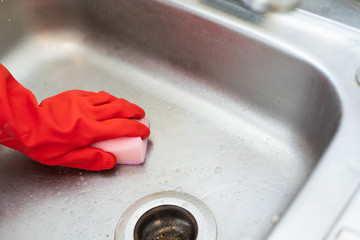 Close up view hand in red cleaning glove using sponge clean the sink in the kitchen.