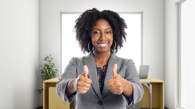 Black African American businesswoman in an office with thumbs up.  She is an owner or an executive of the workplace.  Depicts careers and startup business.