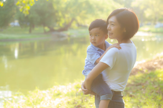 Beautiful Young Asian Mother Carrying Little Boy In The Park, Asia Woman Happy Having Son And Hug Kid, Mom Love And Embracing Child Together In Summer, Mother Day And Family Concept.