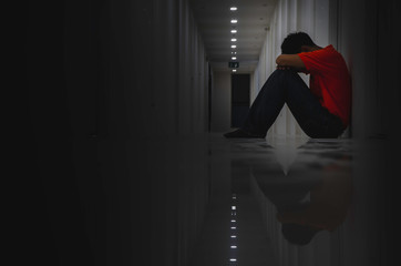 Side view of  Asian young man sitting at the corridor looks disappointed on the floor and looking...