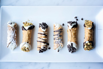 Assorted cannoli desserts decorated with chocolate chips, chocolate and nuts