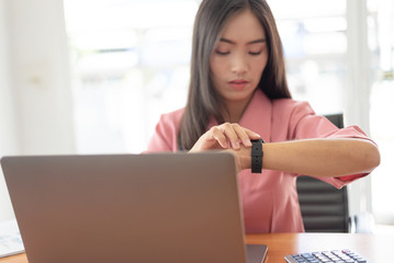 Young asian businesswoman checking the time, work with laptop computer.