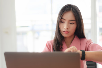 Young asian businesswoman checking the time, work with laptop computer.