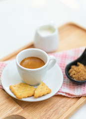 Coffee americano and saucer on a wooden plate with milk.