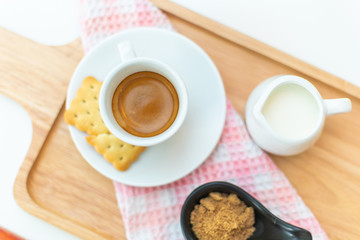 Coffee americano and saucer on a wooden plate with milk. on top