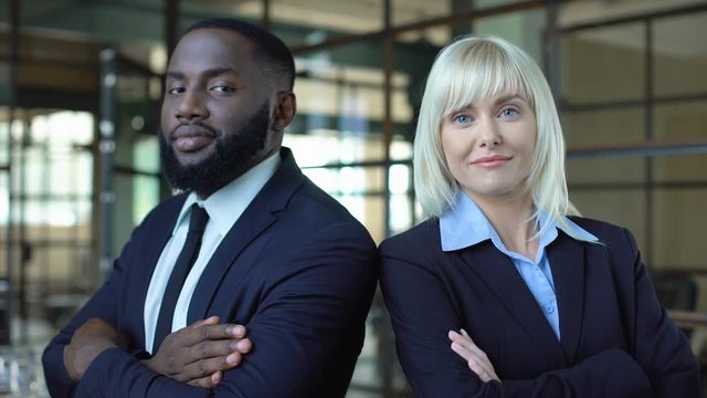 African man and caucasian woman in suits folding arms, professional managers