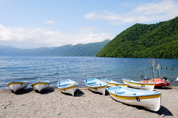 Fototapeta na wymiar Many small fishing boats on the shore on sunny day blue cloud sky with green mountain range and lake view in the morning time ,good weather on the sea or island
