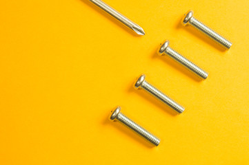 Screws and screwdriver on a yellow background
