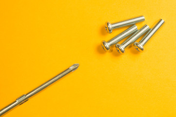 Screws and screwdriver on a yellow background