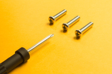 Screws and screwdriver on a yellow background