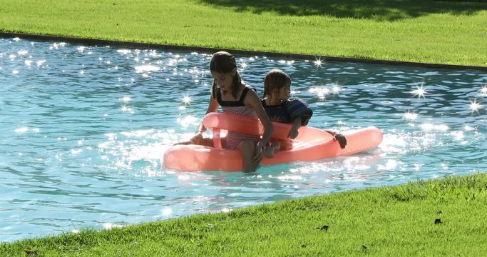 Children playing the swimming pool water on top of inflatable mattress