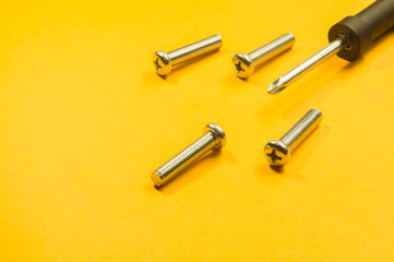 Screws and screwdriver on a yellow background