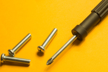 Screws and screwdriver on a yellow background