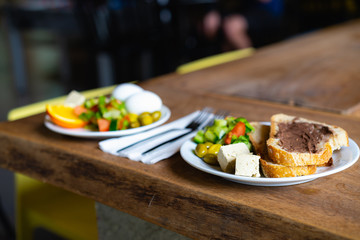 Breakfast food on a rustic table edge with bread, olives and healthy salad