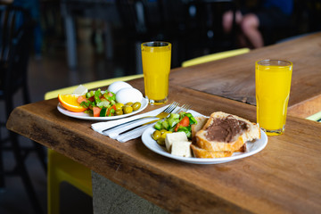 Breakfast food on a rustic table with orange juice, bread, fresh salad and fruit