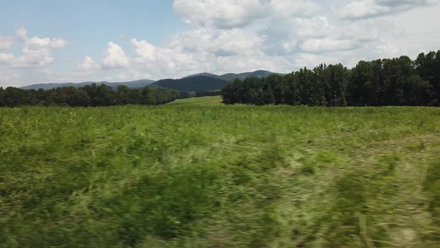 Driving past a rolling grassy plain with trees in the background and mountains on the horizon in slow motion